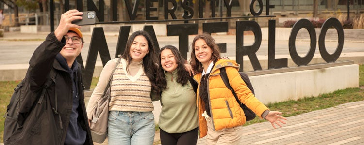 Four students taking a selfie together in front of the Waterloo sign