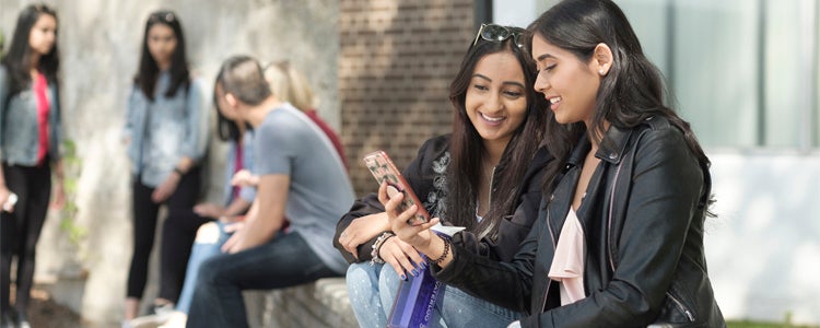 Two students sitting outside and looking at a cell phone