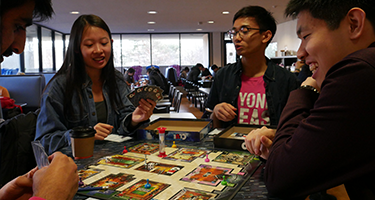 Three students sitting at table playing a board game