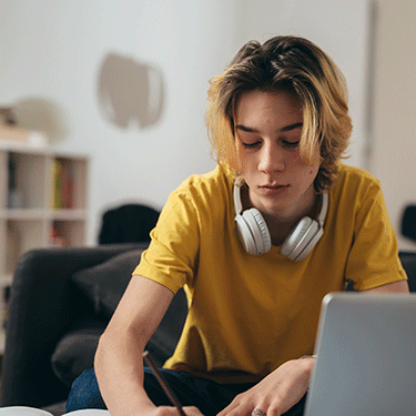 Student in yellow shirt and headphones sits in front of a laptop