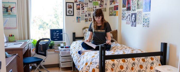 Waterloo student reading a book on their bed in a St. Jerome's University residence room.
