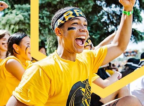 A student in a gold shirt and headband cheers with other students