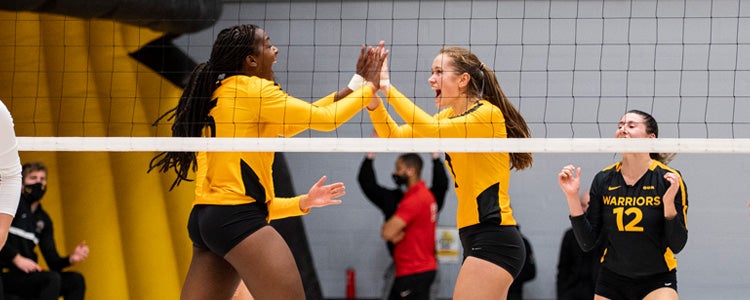 Two students on the women's volleyball team high fiving