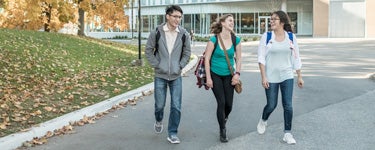 3 students with backpacks walk on sidewalk