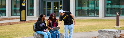 Students sitting outside outside a glass-walled building at the University of Waterloo