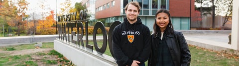 Two students stand in front of a University of Waterloo sign