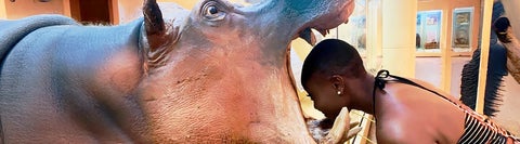 Akua placing her head inside the mouth of a hippo statue.