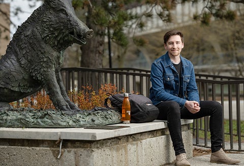 student sitting on low concrete wall in front of statue of a boar