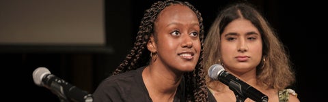 A student looking up and talking through a microphone stand on a stage.