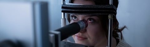 Woman undergoing eye exam, looking at camera while using machine.