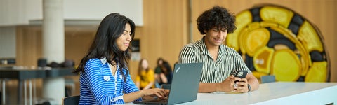 Students with laptop and phone at desk in bright atrium at the University of Waterloo