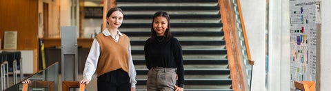 Two students walking down a staircase wearing business casual clothing