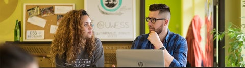 two students talking sitting in a bright study space in front of laptop