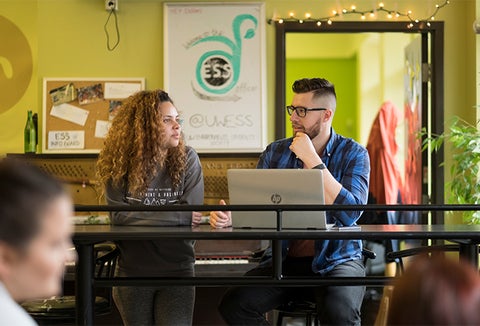 two students in a bright study space talking in front of laptop