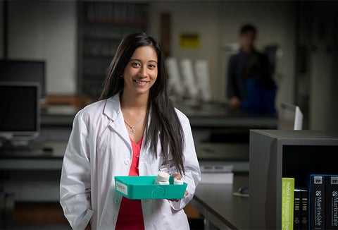 student in a lab coat standing with pharmacist bottles in a green tray