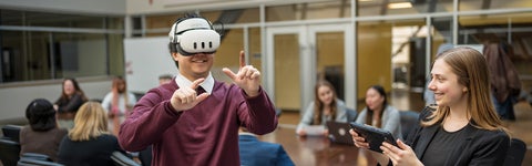 Student wearing a VR headset in an office with people in the background
