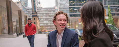 Two people in business attire sitting and talking on a city street.
