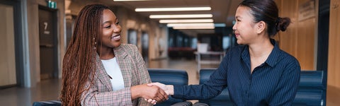 Two students in business clothes shake hands and smile