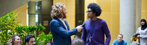 One student being interviewed by presenter with a mic in front of a smiling crowd