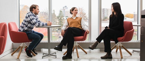Three students sit in discussion in front of a window