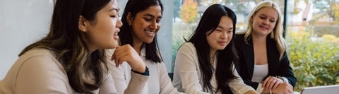Four students sitting at a table and looking at a laptop.