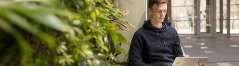 student sitting by plants using laptop