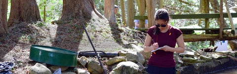 Student writing in notebook while standing in shallow stream