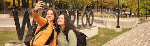 Two students taking a selfie in front of a University of Waterloo sign