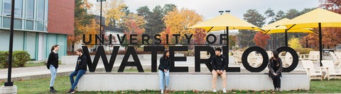 Five students sitting on the University of Waterloo sign on Waterloo's campus