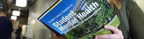 Student reading a book titled "Student Mental Health"