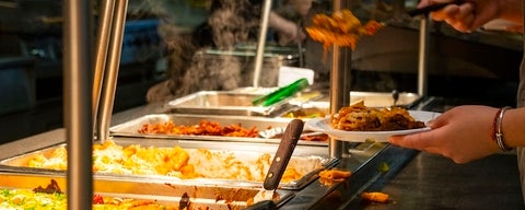 A person's hands putting hot food onto their plate.
