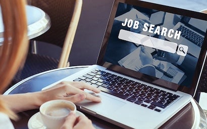 A person holding a cup of coffee with a job search bar on their laptop.