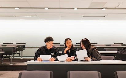 Three students sitting on a table holding pieces of paper.