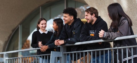 Five students leaning on a railing outside