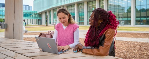 Two students sitting on at a table outside looking at a laptop