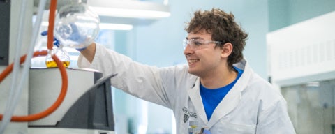 Student pouring liquid from a flask in a lab.