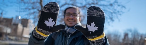 Indian student holding up mittens with the maple leaf logo on them