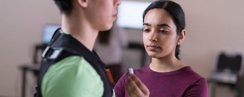 A student examining a device while assisting another person in a lab