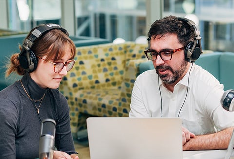 two people looking at computer screen wearing headphones
