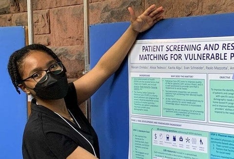 Mariam stands before an infographic about patient screening