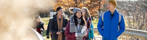 Students in winter coats and hats walk across a small bridge