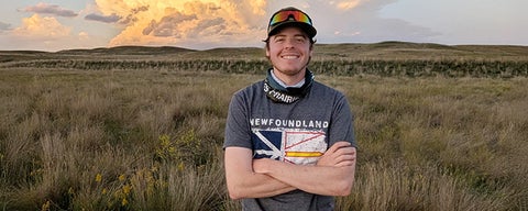 Matthew smiling in a field with a beautiful sunrise behind him.