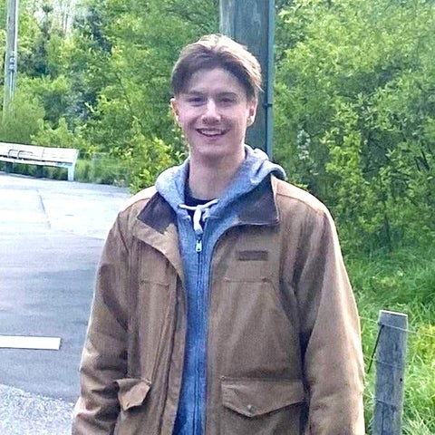 Nathan smiles while wearing a hoodie and jacket outside