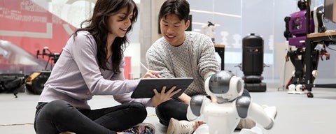Two students sitting on floor with small robot in front of them