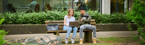 Students look at a laptop while sitting on a bench at the University of Waterloo 