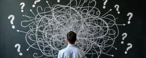 A man facing a chalkboard with many arrows going in different directions and question marks.