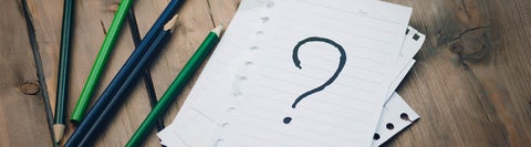 large paper sheet with question mark drawn on it sitting on a wood table