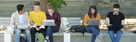 students sitting on a bench using computers