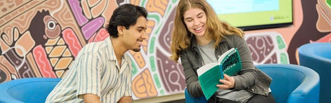 Two students leaning in and looking at a book
