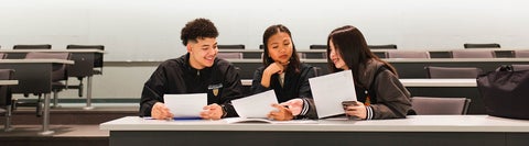 Group of three students in a classroom with papers in hand